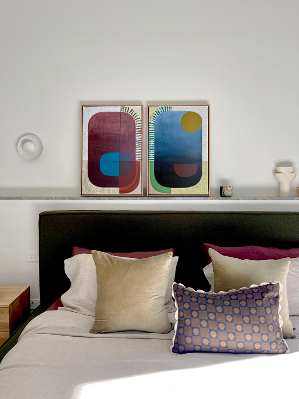 Bedroom with colorful abstract art on the wall above a bed with patterned pillows.