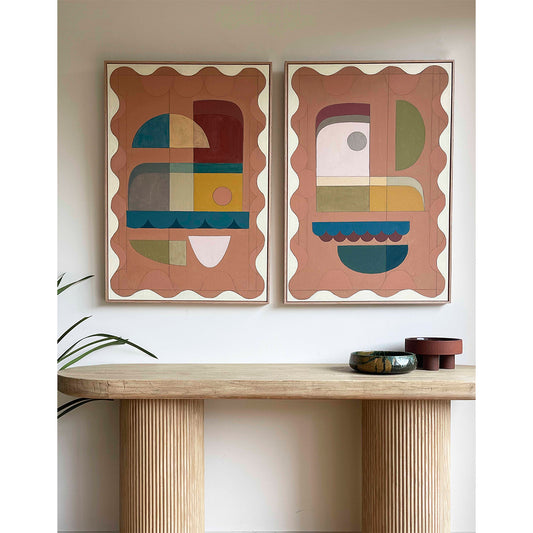 Two framed abstract giclee prints with a terracotta color border and geometric shapes inside, displayed above a wooden table with decorative objects on it.