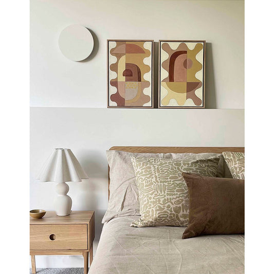 Two framed abstract artworks with a wavy motif in blush and warm colors, hanging above a bed in a minimalist bedroom setting.